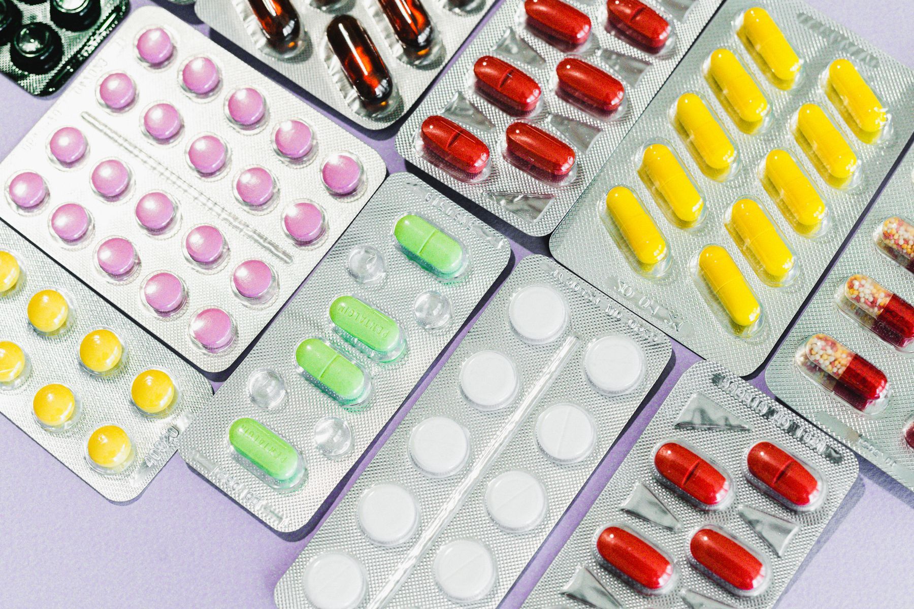 Tablets and capsules in blister packs on a lilac surface